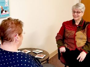 Sister Patrice seated in a chair talking with a colleague