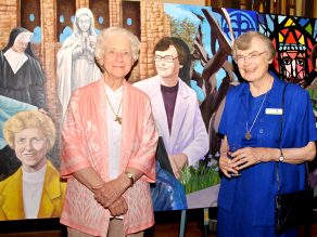 SIsters stand infront of their depictions on anniversary mural