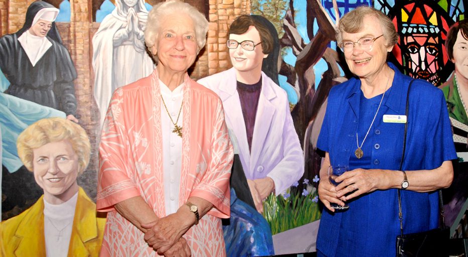 SIsters stand infront of their depictions on anniversary mural